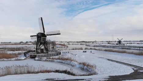 aerial: winter snow, traditional dutch windmills and frozen canal polder land