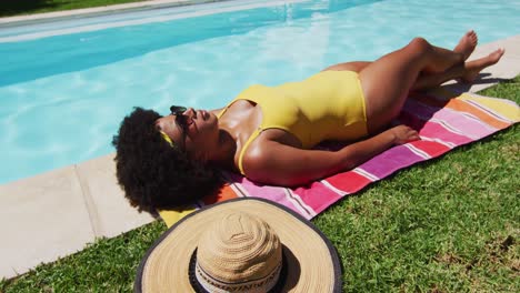 Mixed-race-woman-lying-on-blanket-sunbathing-by-the-pool