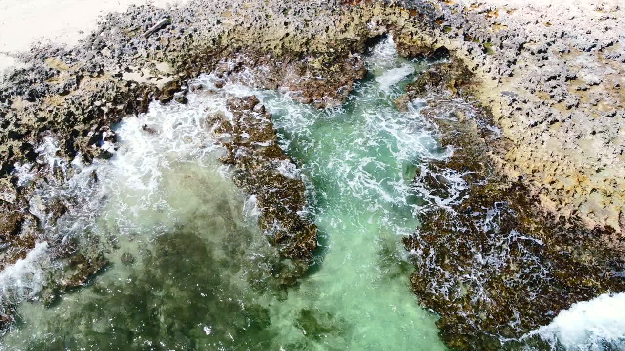 olas cristalinas rompiendo en la costa rocosa de coral en cozumel méxico en un día soleado, antena de arriba hacia abajo