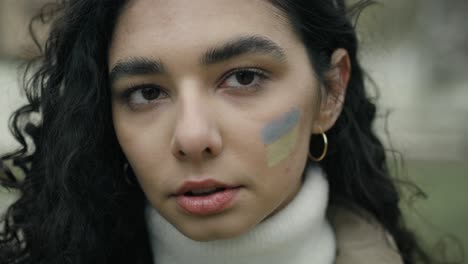 close up portrait of young woman with ukrainian flag painted on her cheek.