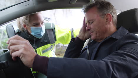 female paramedic wearing face mask helping injured male driver involved in road traffic accident