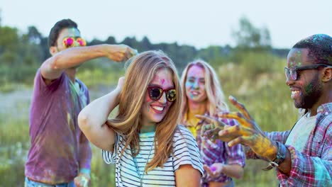 razas mixtas jóvenes alegres en pinturas coloridas bailando juntos y celebrando el festival holi afuera