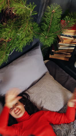 attractive girl in red on bed with gifts. cheerful young woman enjoying spare time while laying on bed in christmas decorated bedroom. top view. vertical video