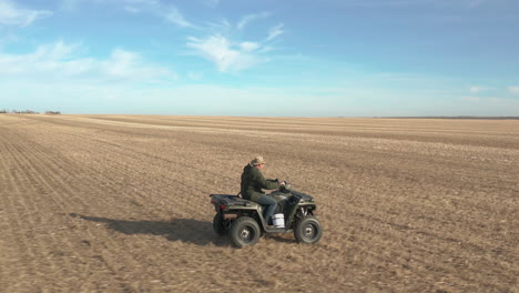 farmer-driving-on-his-quad-in-vast-farmland,-aerial-follow