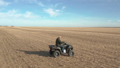 farmer driving on his quad in vast farmland, aerial follow