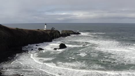 Yaquina-Head-Lighthouse-during-cloudy-rain-day,-landscape-aerial-rising-view,-Oregon-coast