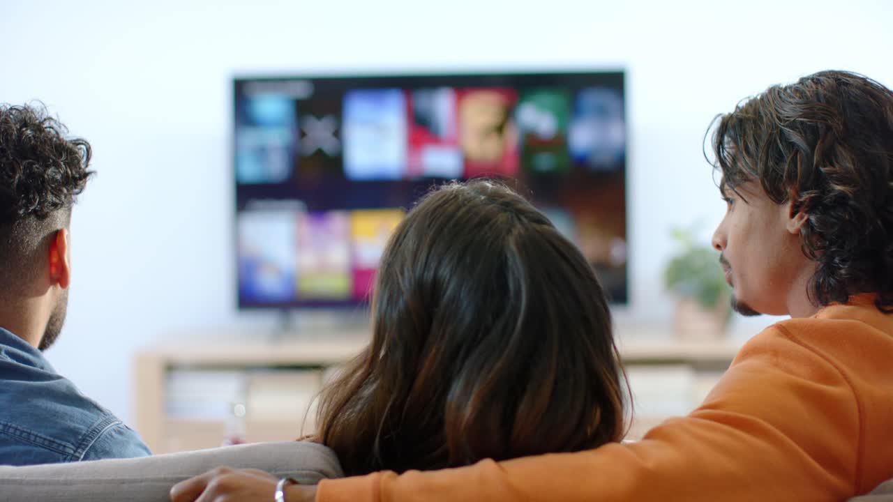 Una coppia e un amico prendono i popcorn e usano il telecomando in salotto prima di scegliere un programma