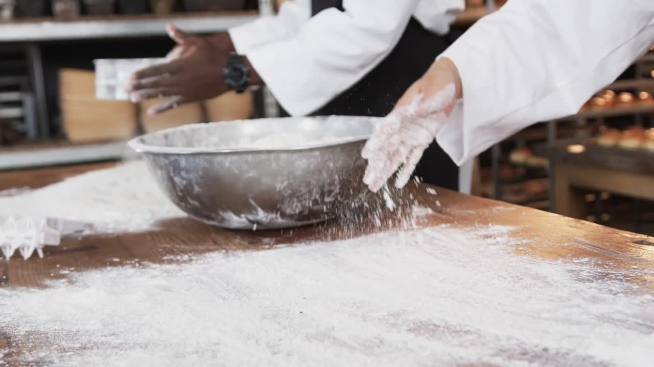 Diverse bakers working in bakery kitchen, spreading flour on counter in slow motion