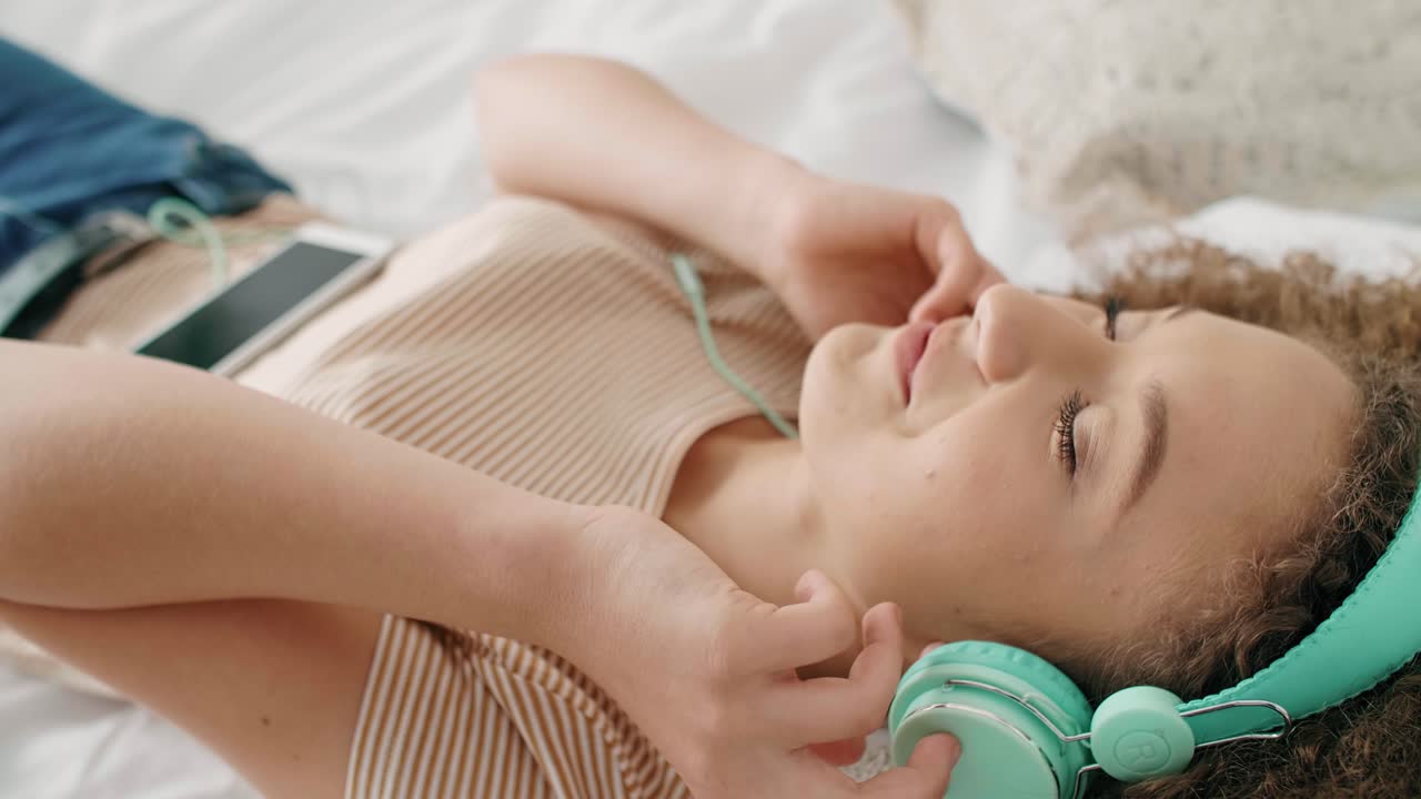 mujer sonriente escuchando música y relajándose en la cama