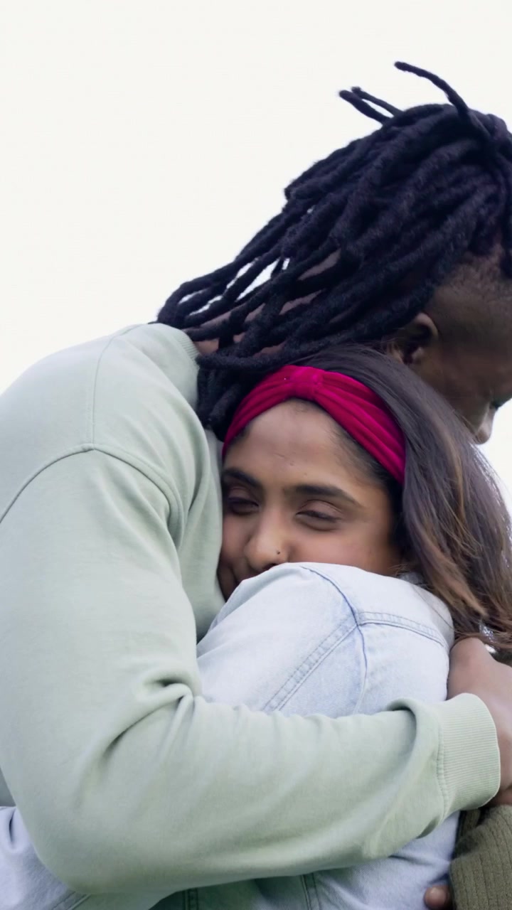 Vertical video: Smiling man adjusting olive-green sweater, hugging woman in park for comfort