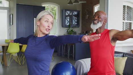 mixed race senior couple performing stretching exercise together at home