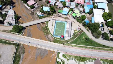 a football soccer pitch, quiet roads, houses and a muddy river after flash floods in dili, timor leste - aerial drone birds eye view