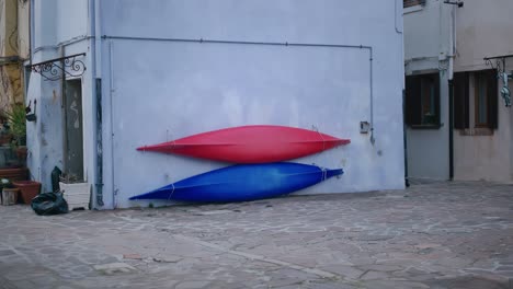 Colorful-red-and-blue-kayaks-mounted-on-a-wall-in-a-rustic-courtyard-on-Burano-Island,-Venice