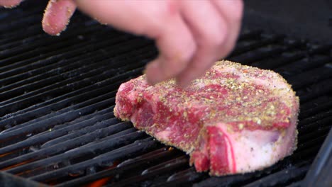 dos manos ponen un grueso filete de costilla crudo en una parrilla comenzando su proceso de asado a cámara lenta