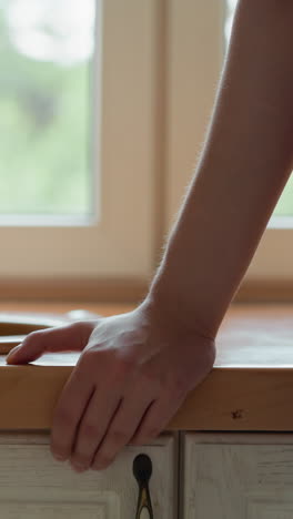 woman stands by kitchen sink with vintage tap closeup. maid looks through window after housework finishing in apartment. domestic chores routine