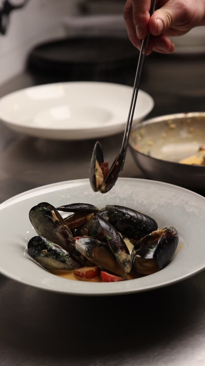 Chef Plating Fresh Mussels with Tongs in a Restaurant Kitchen