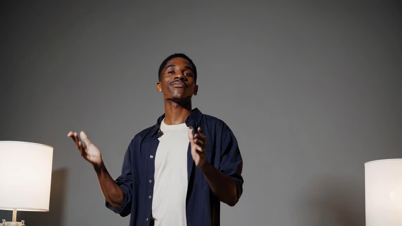 A mid-shot video captures a person gesturing expressively in a minimalist setting with soft