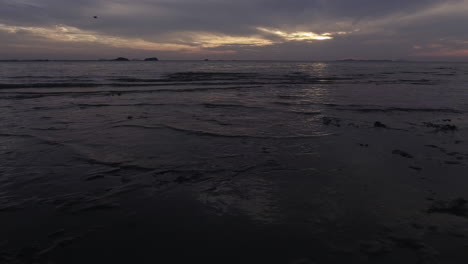 low tide, thin waves coming into the beach, sunset, object of interest, drone shot