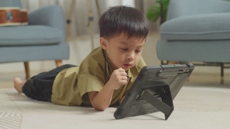 close up of asian kid lying on the floor watching movie on a tablet at home