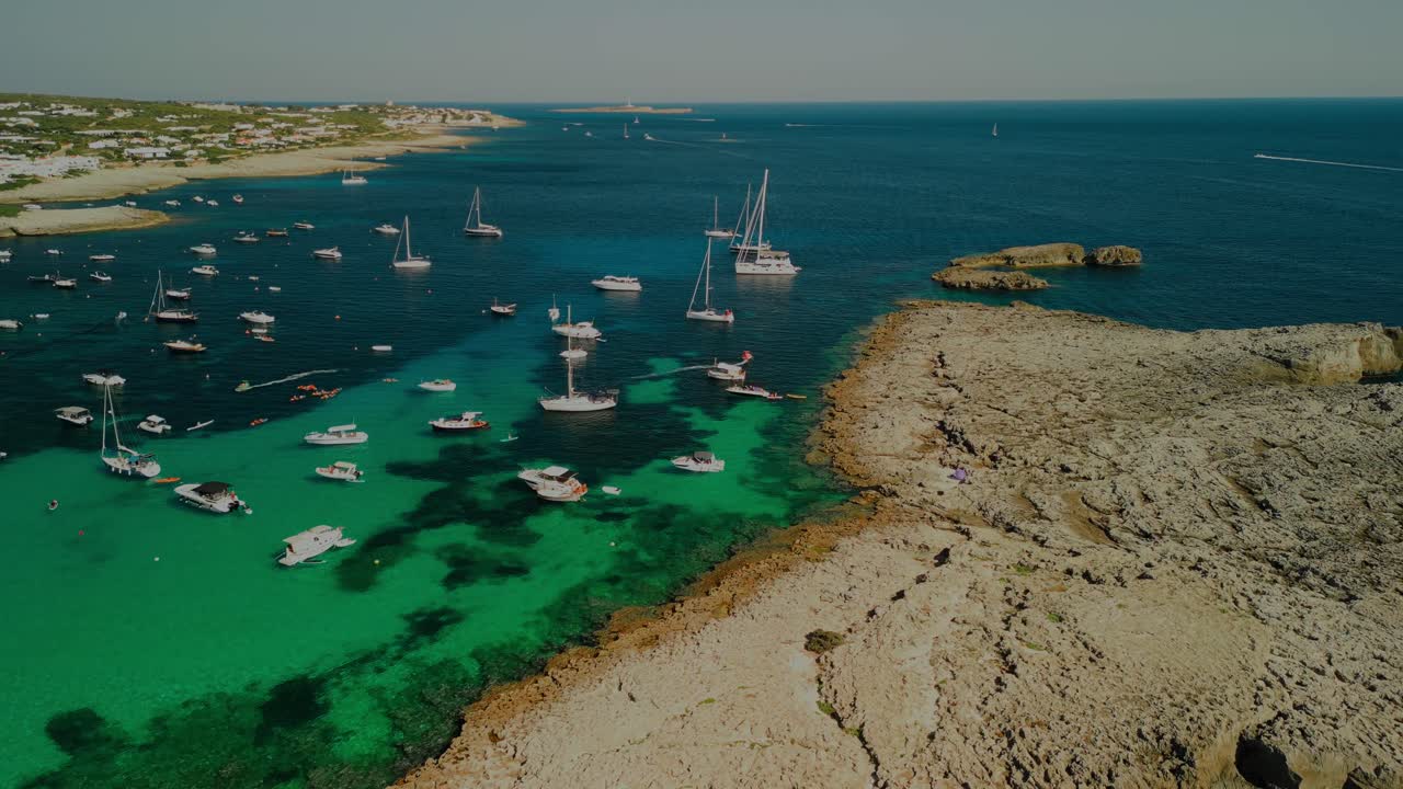 Boats anchored in vibrant blue bay of Menorca near sandy beach and shallow reef edge, ascend overview