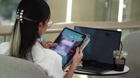 young woman interacts with tablet near laptop and drink