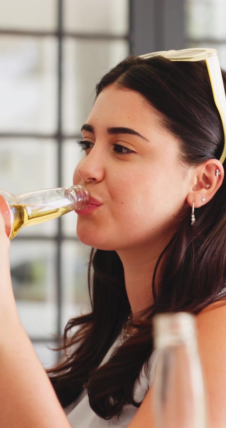 Young Woman Laughing and Drinking from a Glass Bottle