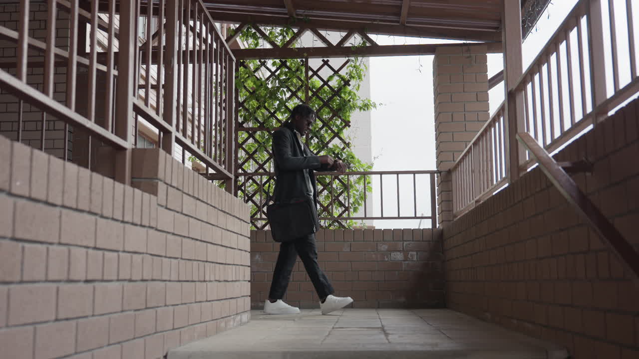 Gentle man leaves room into hallway while checking wrist watch, glancing at time with focused expression, smart casual outfit, purposeful step, doorway and interior light suggest office departure