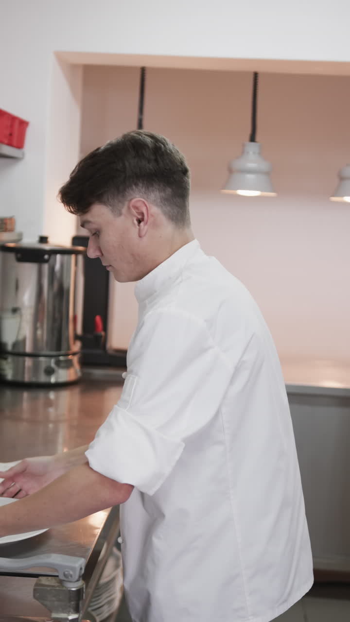 Caucasian male chef putting plate on counter and crossing arms in kitchen, slow motion, vertical