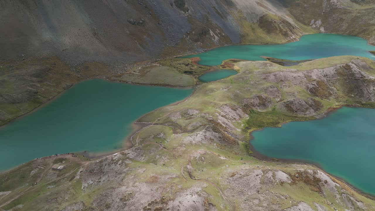 Drone footage of three stunning turquoise lagoons nestled in the mountains of Ausangate, with soft light and shadows under a cloudy yet luminous sky