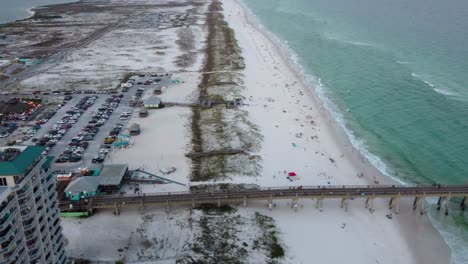 aerial view of crowded beach with pier and parking lot