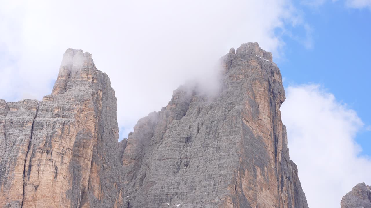 Tre Cime di Lavaredo mountain peaks cut through fog and clouds in Dolomites, Italy