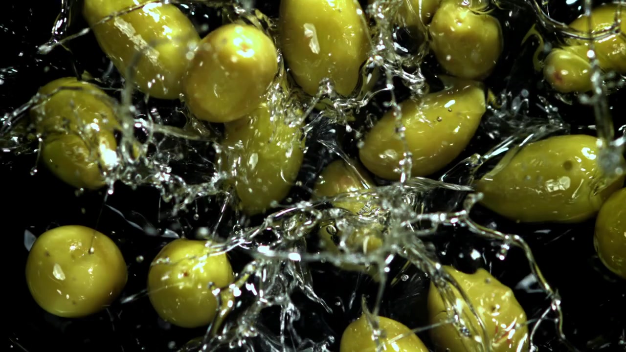 Olive verdi che cadono e schizzano nell'acqua al rallentatore.
