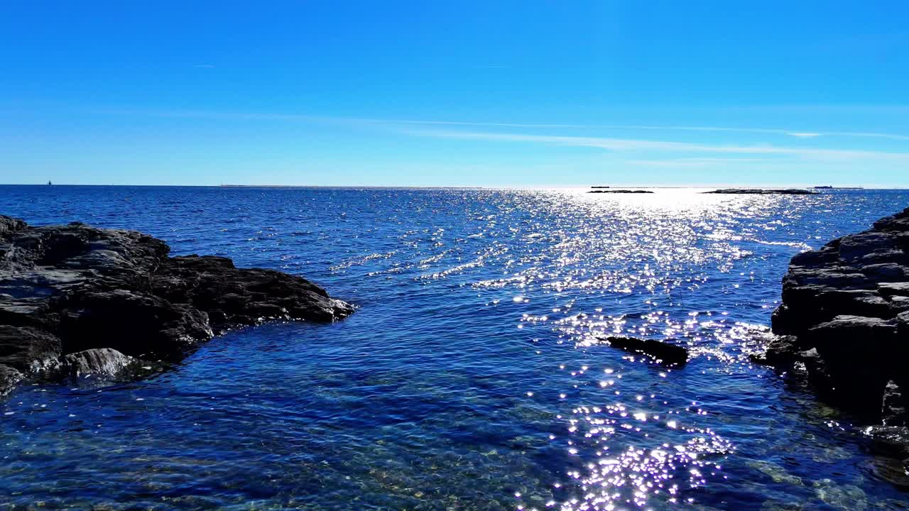 Sunrise over the rocky coastline with shimmering water reflections and clear blue skies along the horizon, capturing a serene and peaceful coastal morning