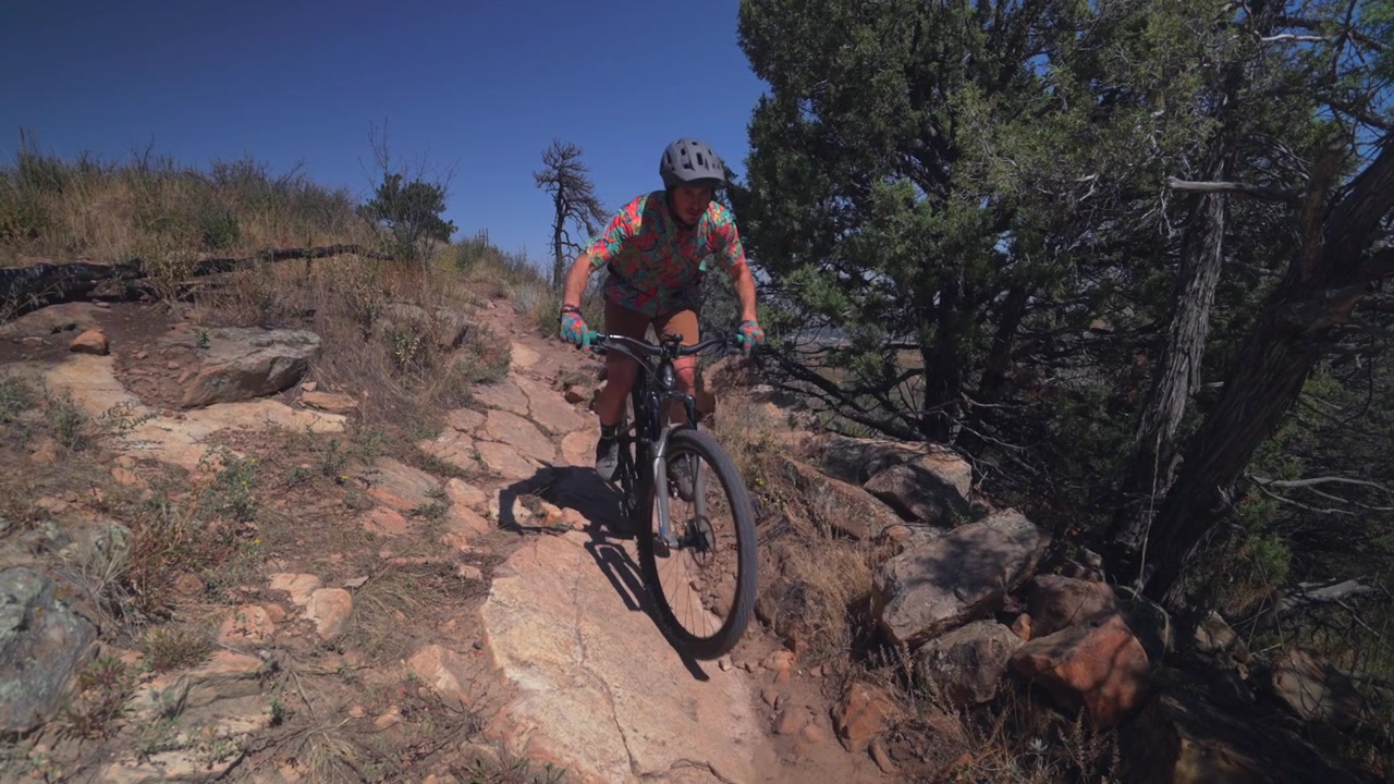 Ciclista adulto de mountain bike em descida com quedas de pedras em Red Rocks, Morrison, Golden, Colorado. Imagem estática da Trilha Dinosaur Ridge e Dakota Ridge. Esporte e fitness nos sopés de Denver, Front Range, em um dia ensolarado.