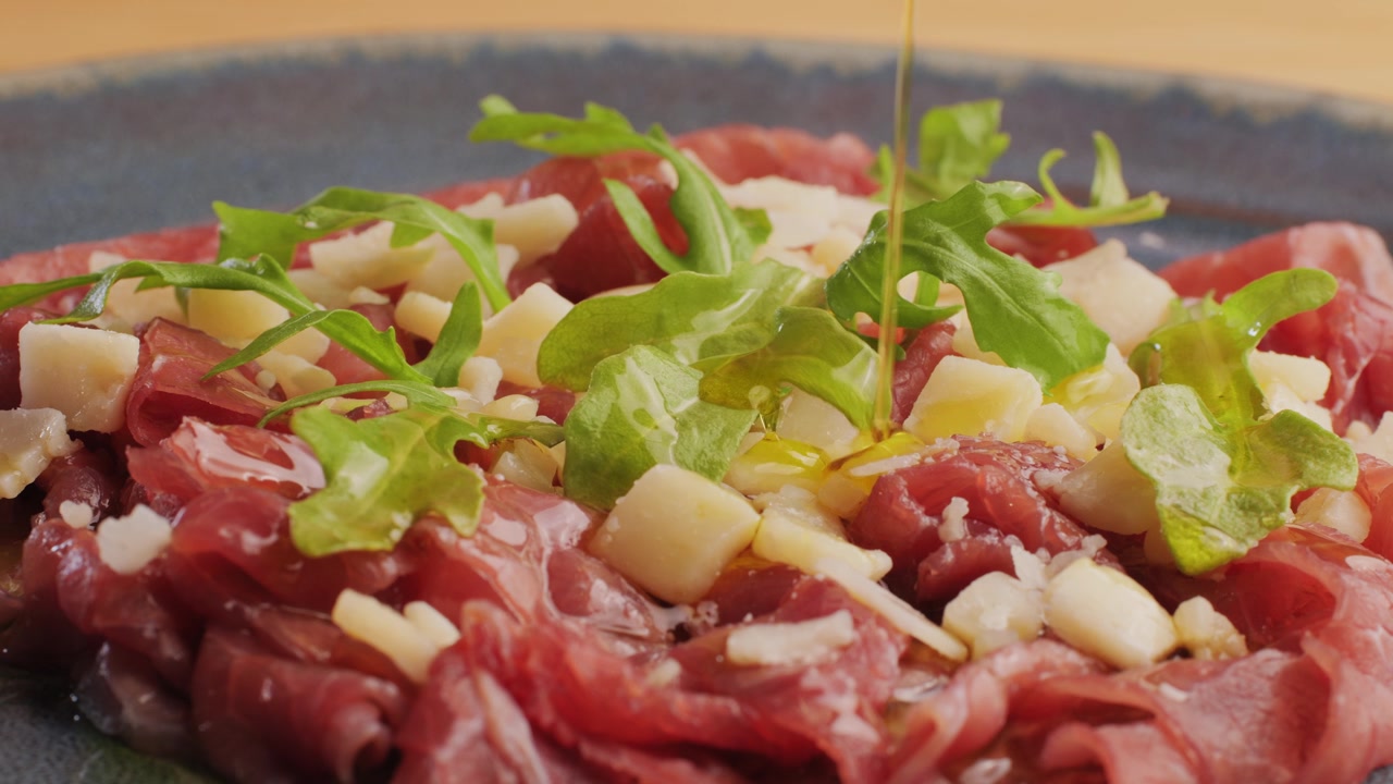 Olio d'oliva versato a filo su carpaccio di manzo con Parmigiano e rucola