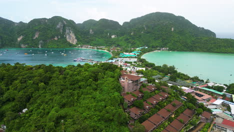 aerial rising overview of villas on hillside of koh phi phi to deep blue bay with yachts anchored