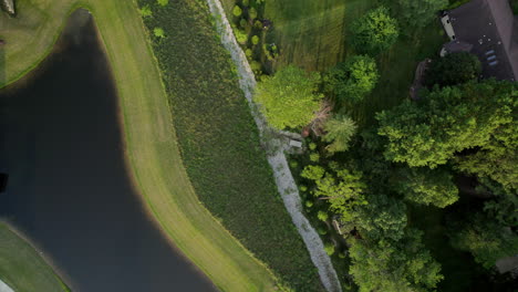top down overhead pull down a small park with a pond and dock and path at golden hour in town and country in st