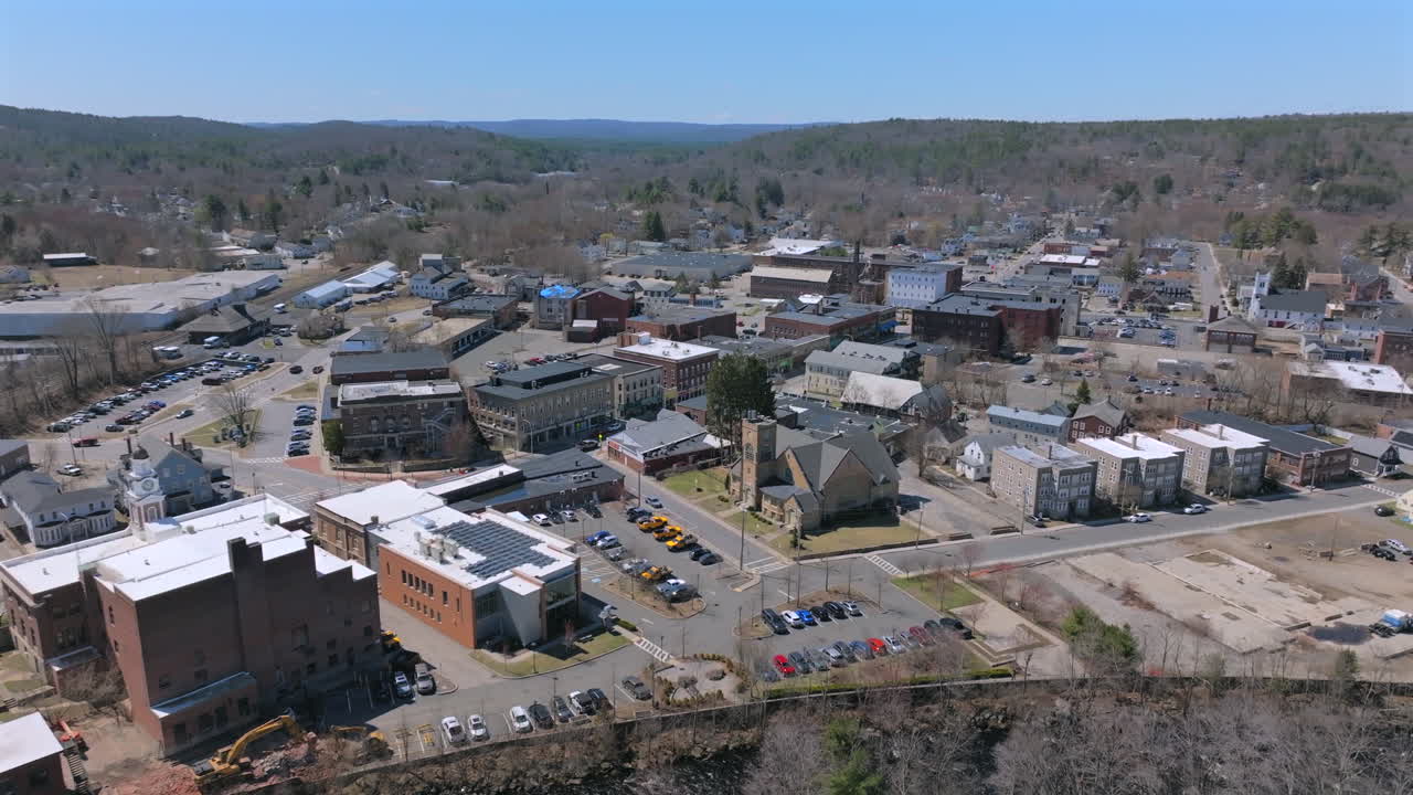Drone aerial view of New England town Athol, Massachusetts in late winter to early spring. Classic buildings, rolling hills, and a riverbank, blending architecture with scenic natural surroundings.