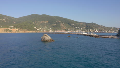 Aerial:-Flying-towards-a-big-rock-in-the-middle-of-the-blue-clear-and-tranquil-sea-near-Skopelos-island-harbor