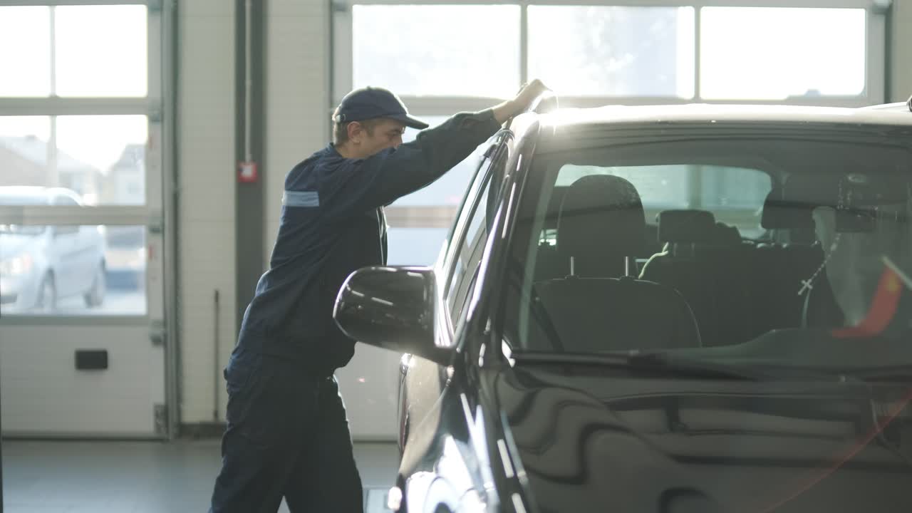 mecánico de automóviles en un uniforme azul empujando un coche dentro de un taller de reparación. el vehículo se está moviendo para mantenimiento o diagnóstico en un taller profesional