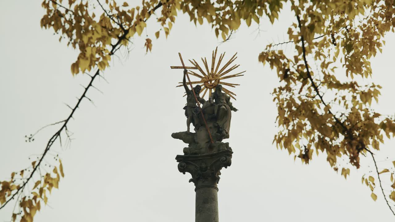 religious monument with golden rays framed by autumn branches in Bratislava