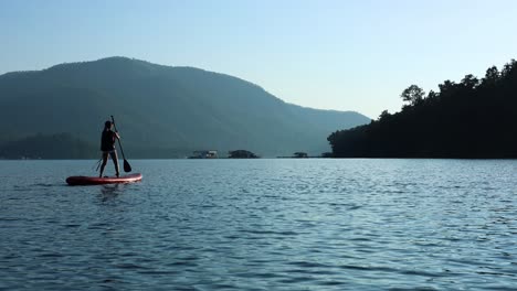 person paddleboarding on calm water at dusk