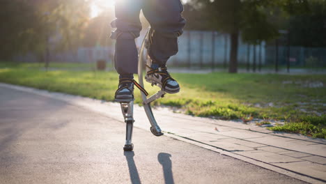 person walking on spring stilts outdoors on paved park path, wearing dark pants and white sneakers, captured from slightly low angle. active movement and bouncing