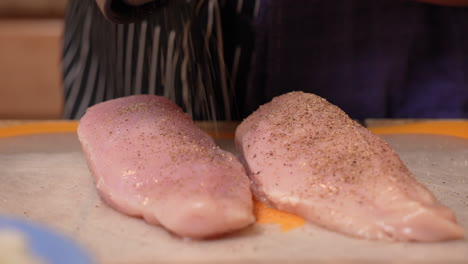 peppering skinless, boneless chicken breasts using a grinder in preparation for cooking them