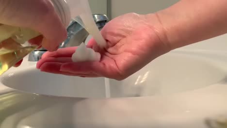 female hands turning on the bathroom faucet and using foam soap to thoroughly wash hands over the sink. the best everyday practice that can kill covid19 (coronavirus) and stop the spread of germs.