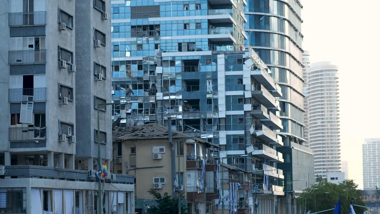 A modern high-rise in Tel Aviv shows shattered windows after an Iranian missile strike, flags visible below