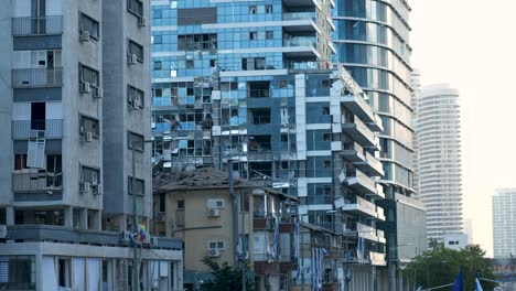 a modern high-rise in tel aviv shows shattered windows after an iranian missile strike, flags visible below