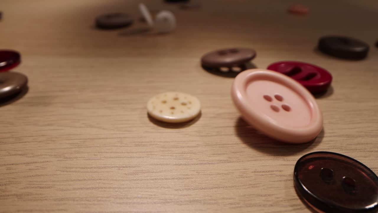 나무 바탕에 떨어지는 바느질 버튼. 옷의 다채로운 버튼이 나무 테이블에 떨어집니다.