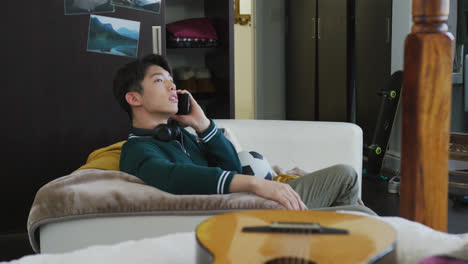 asian boy talking on smartphone sitting on the couch at home