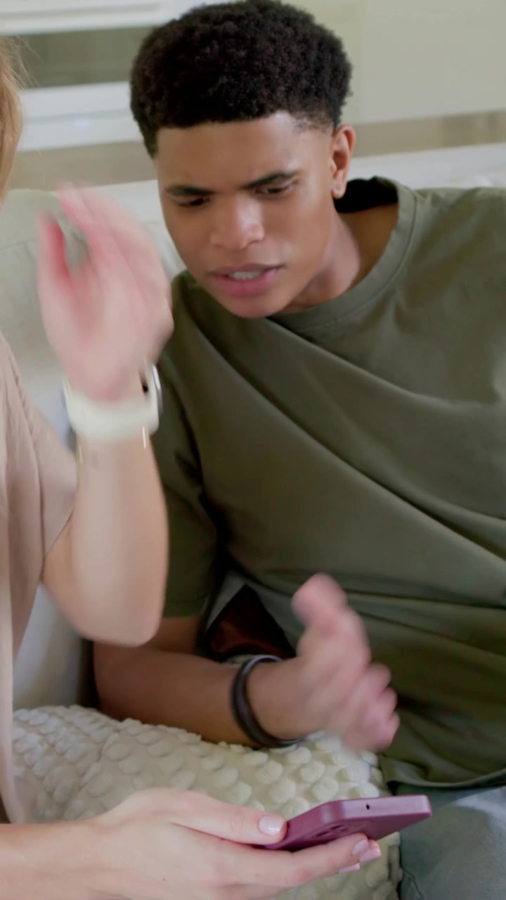 Vertical video: Leaning man in olive tee viewing purple phone at home as woman showing it to learn
